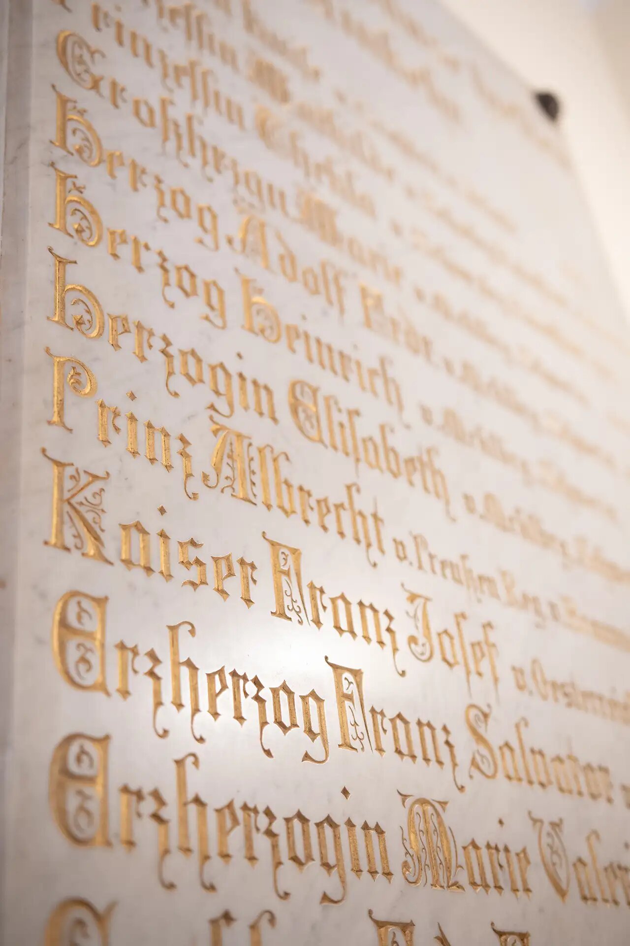 In Marmor gravierte Inschrift mit historischen Namen in goldener Schrift.