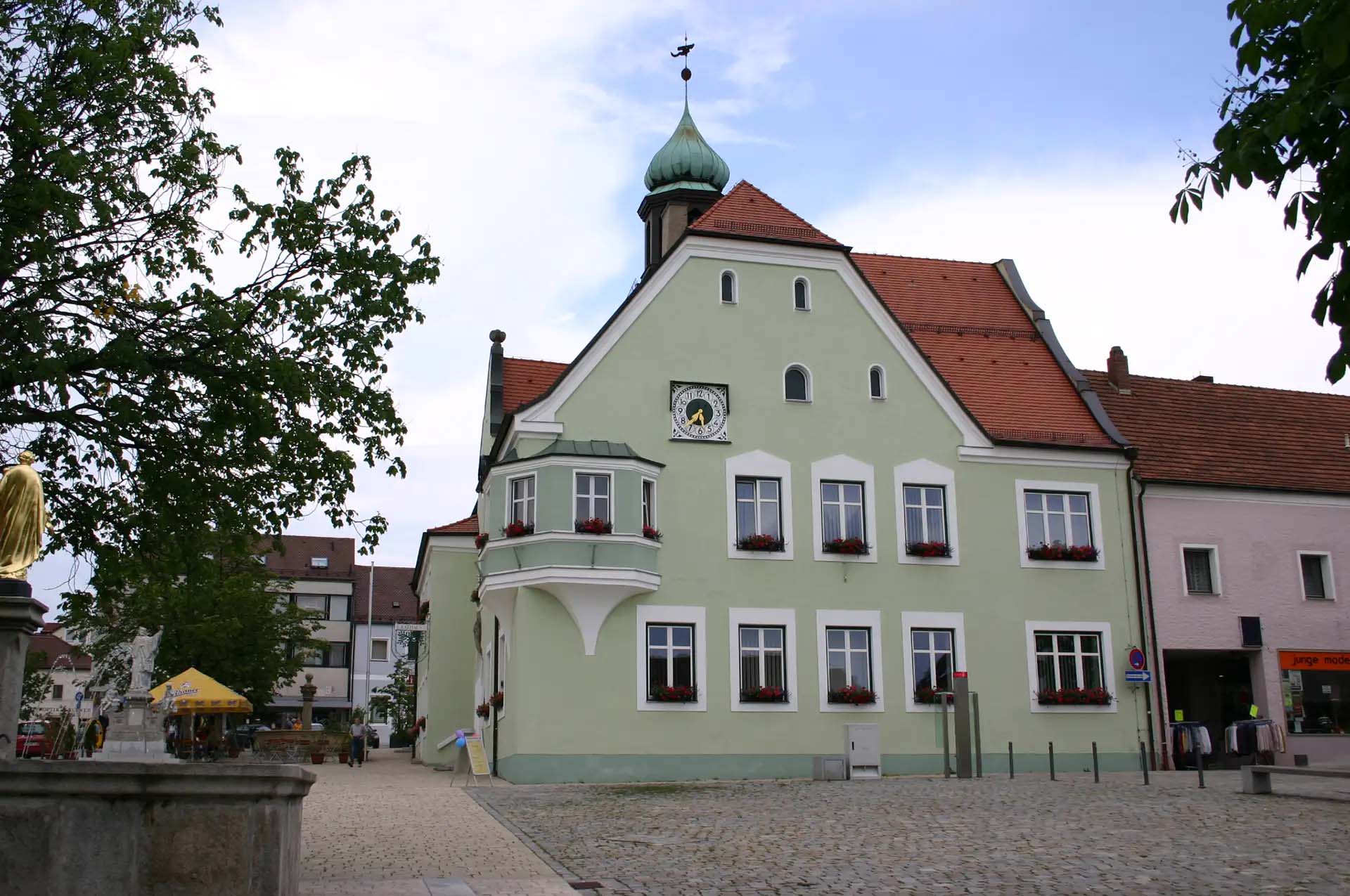 Grünes Gebäude mit Uhrturm, roten Dachziegeln und Blumenkästen.