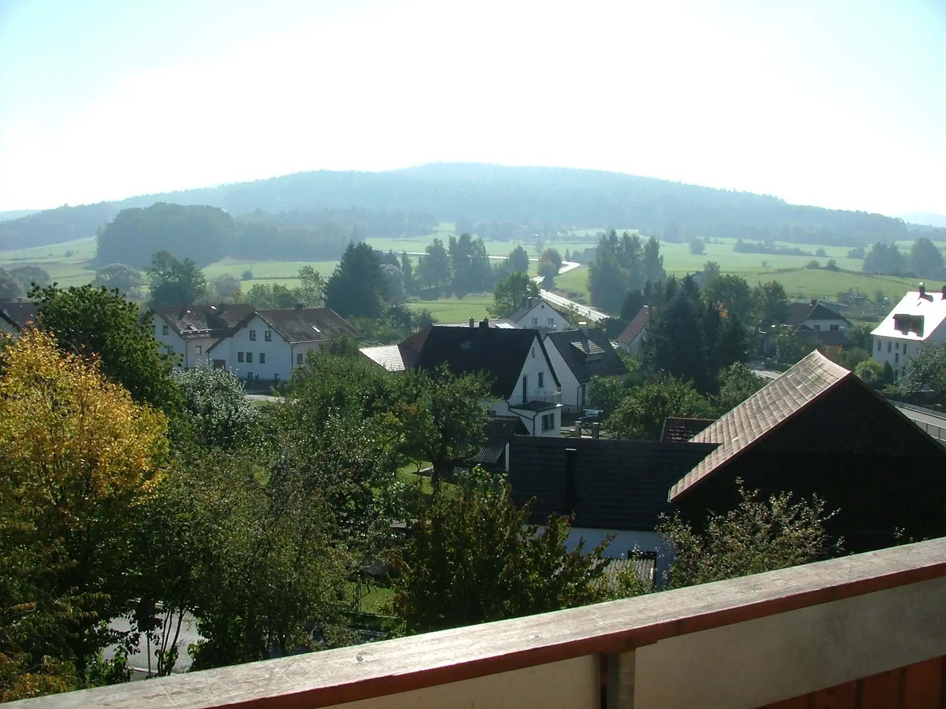 Ländliche Aussicht mit Häusern, Bäumen und Hügeln im Hintergrund.