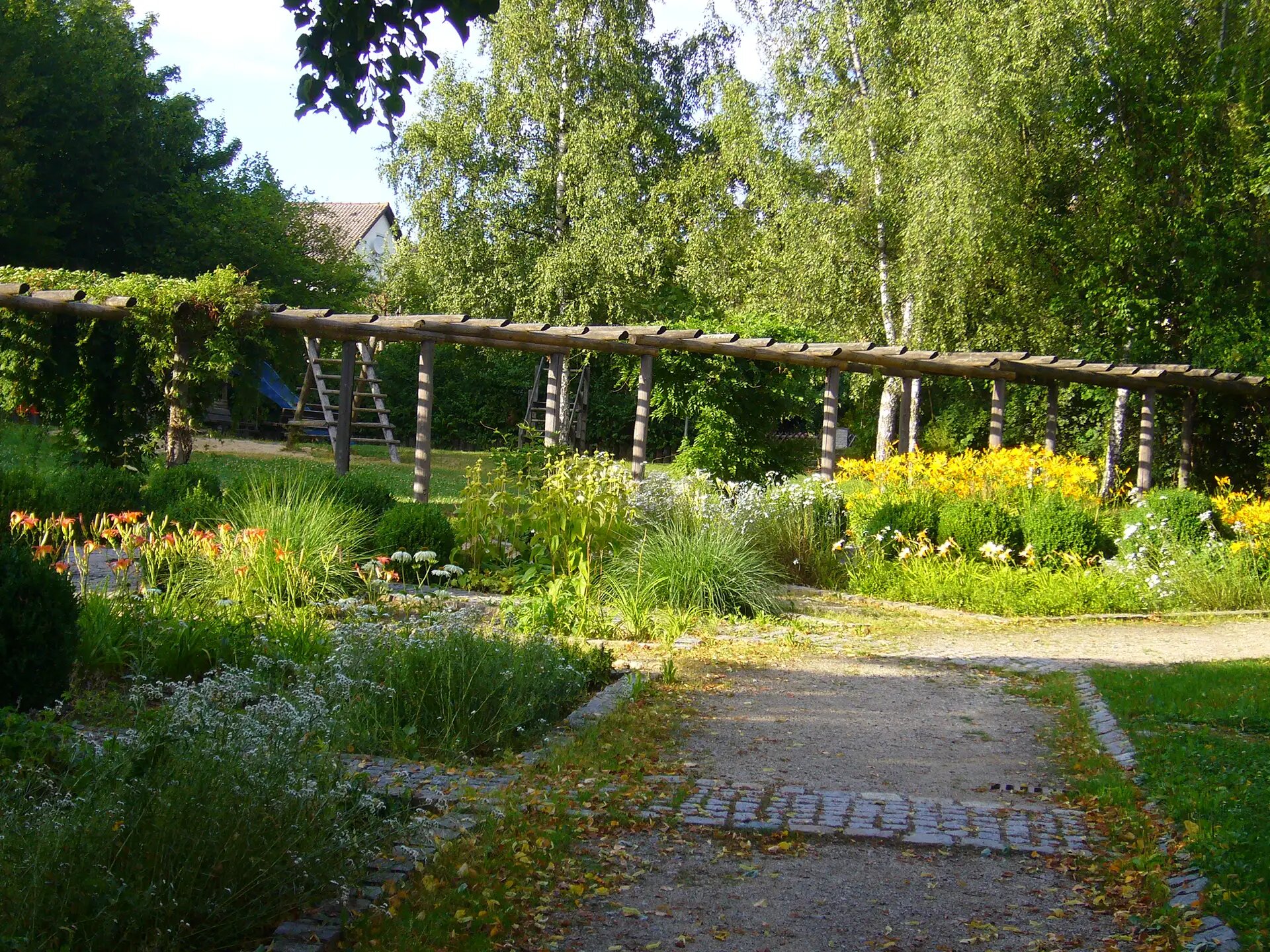 Gepflegter Garten mit Blumenbeeten, Bäumen und Holzpergola.