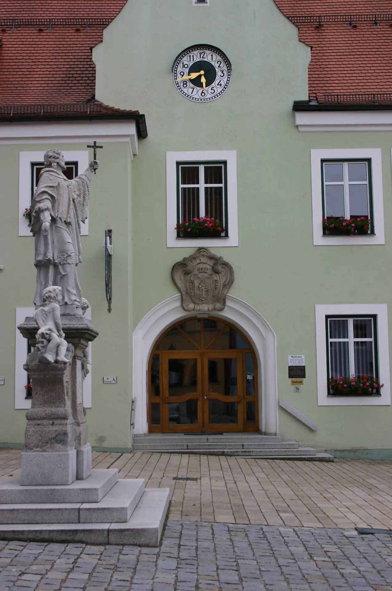 Grünes Rathaus mit Uhr und Statue im Vordergrund.