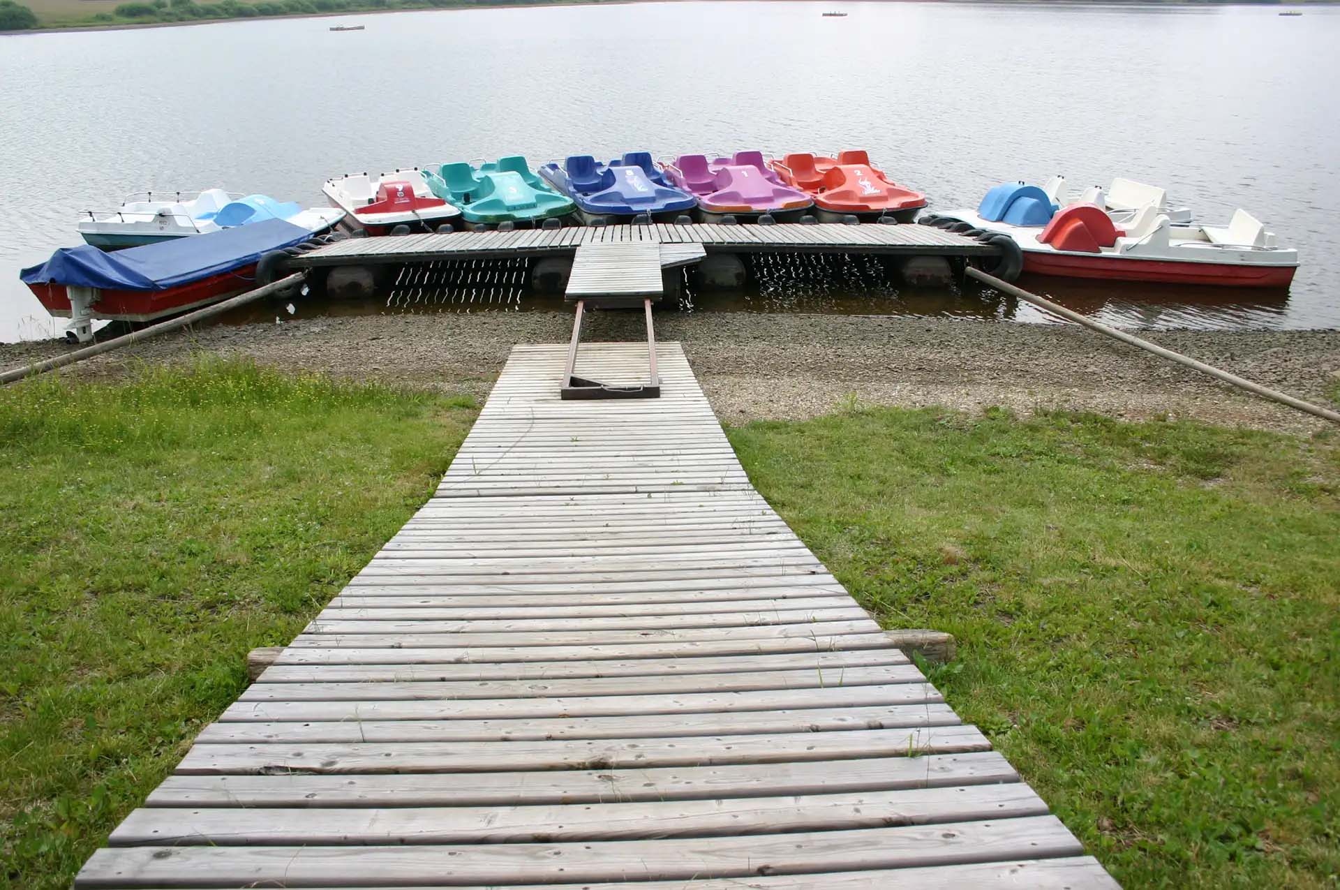 Holzsteg führt zu bunten Tretbooten auf ruhigem See.