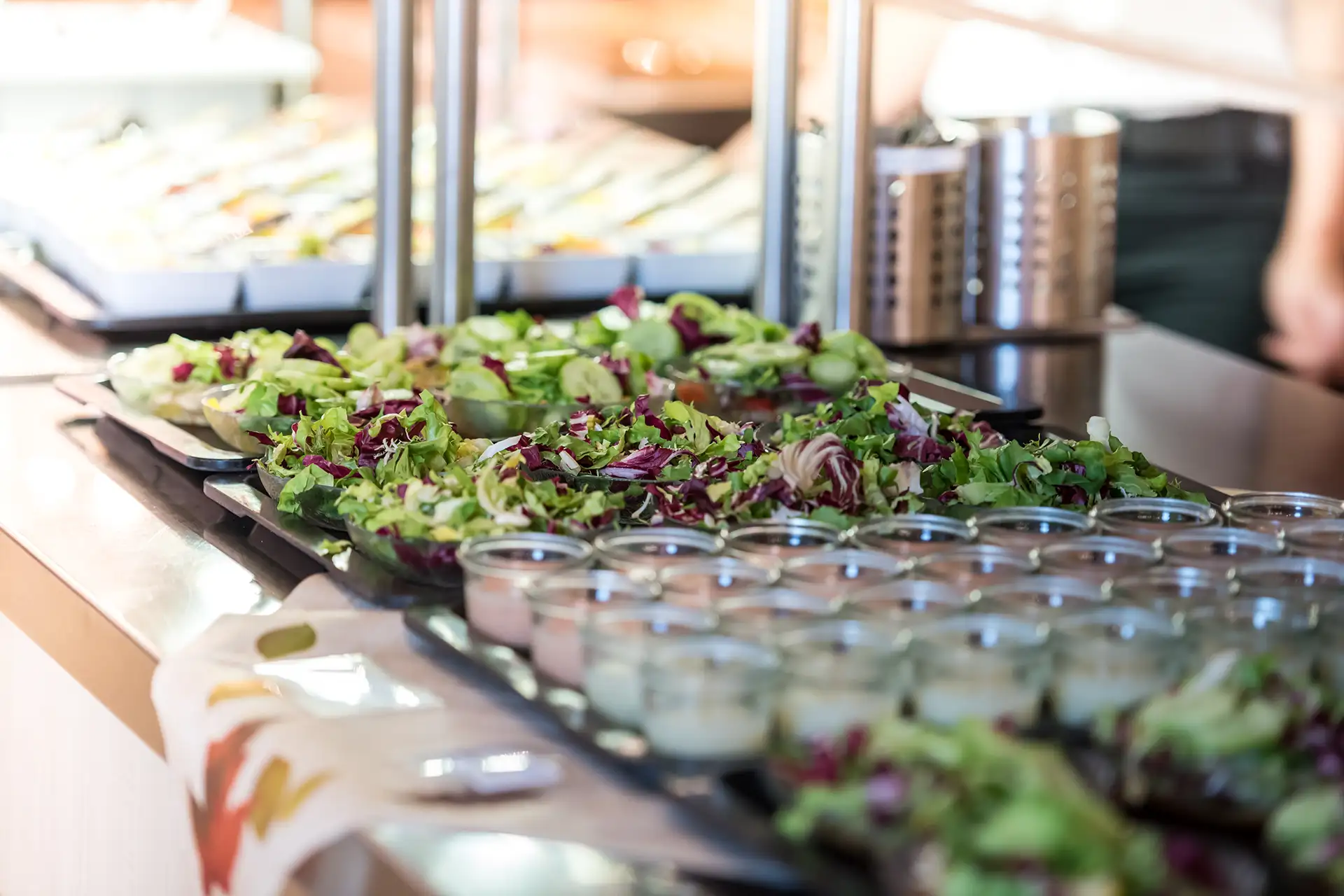 Frische Salatschalen mit Dressings in Gläsern am Buffet angerichtet.