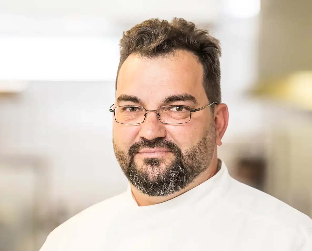 Ein Chefkoch in weißer Kochjacke und Brille, bereit für den Service.