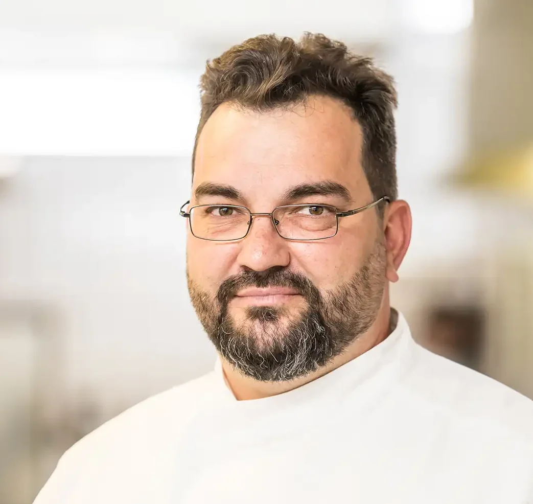 Ein Chefkoch in weißer Kochjacke und Brille, bereit für den Service.