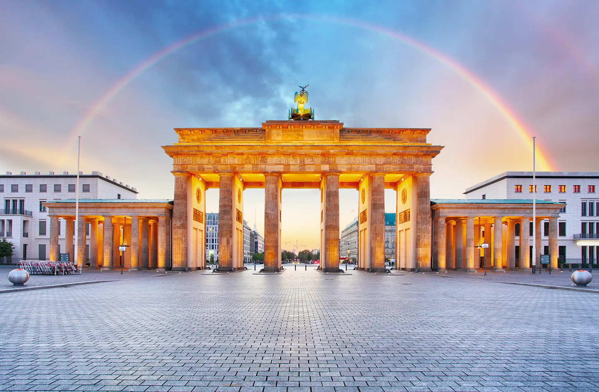 Das Brandenburger Tor in Berlin bei Dämmerung, stimmungsvoll beleuchtet mit einem Regenbogen im Hintergrund.