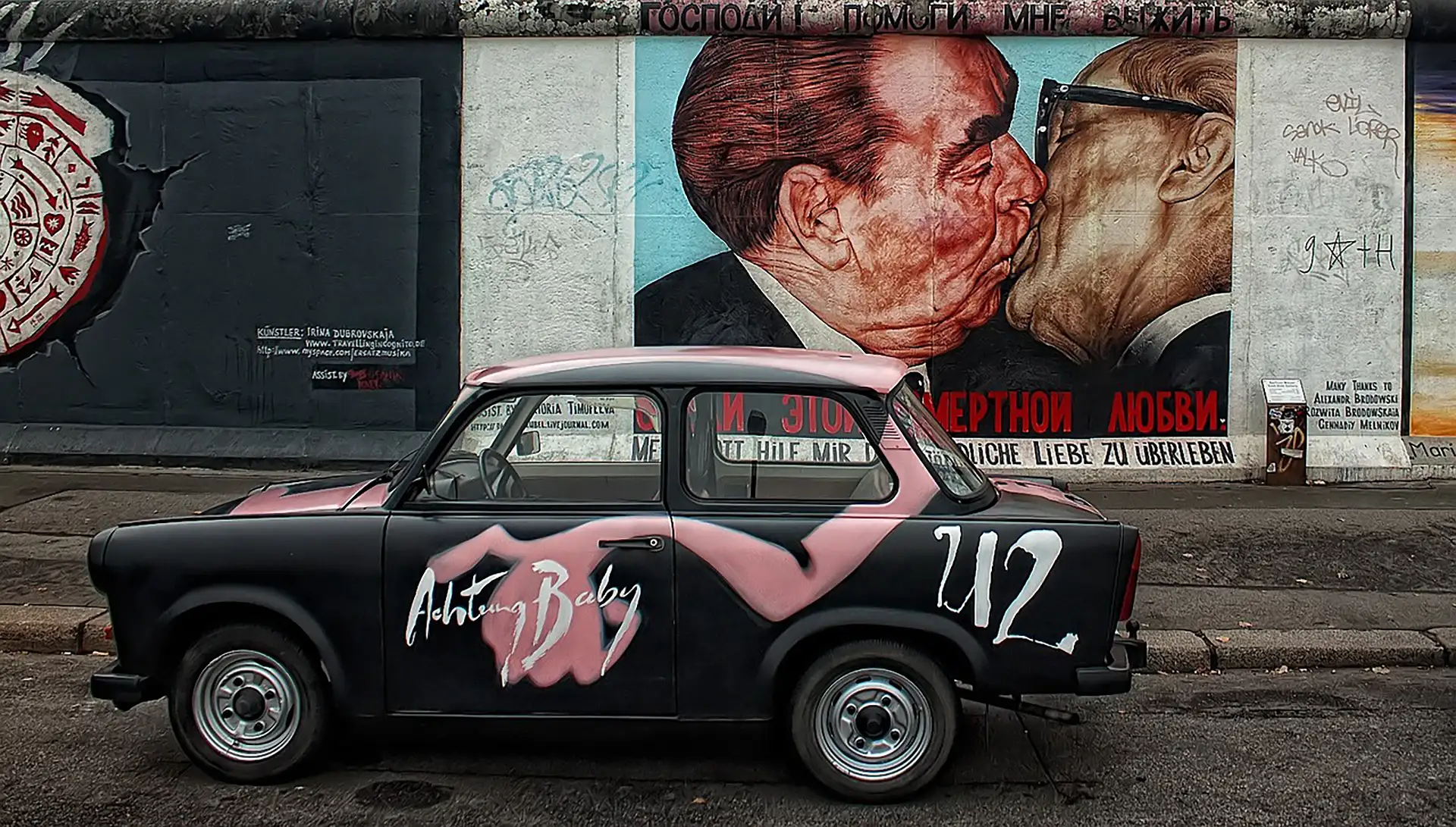 Ein Trabant vor der East Side Gallery, mit berühmtem Bruderkuss-Graffiti.