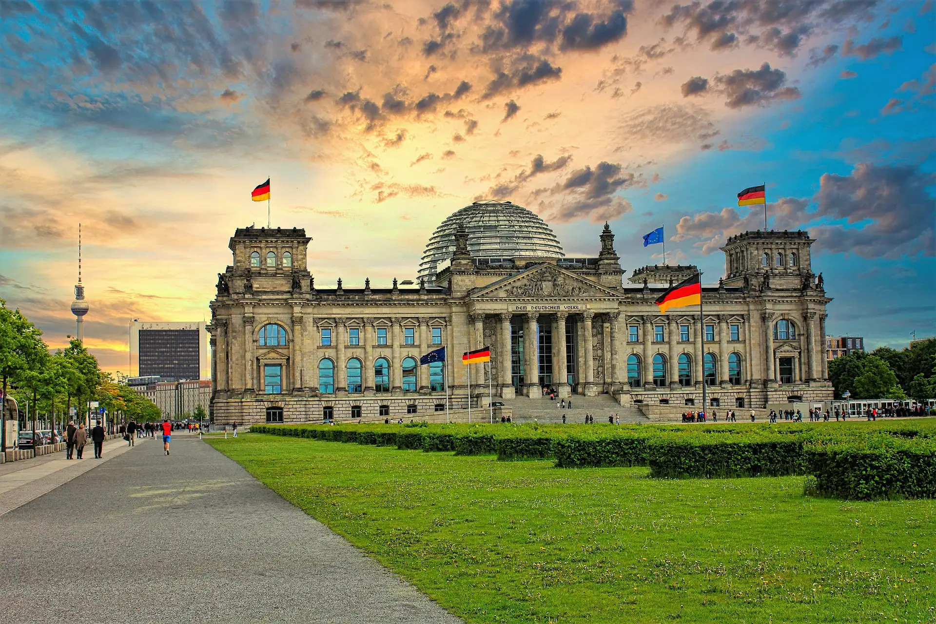 Reichstagsgebäude in Berlin bei Sonnenuntergang, deutsche Flaggen, grüne Wiese.