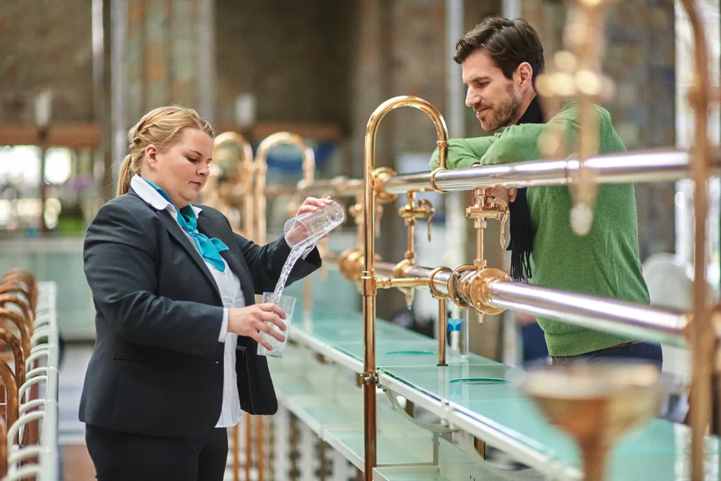Frau füllt Glas mit Wasser aus einer traditionellen Brunnenanlage.