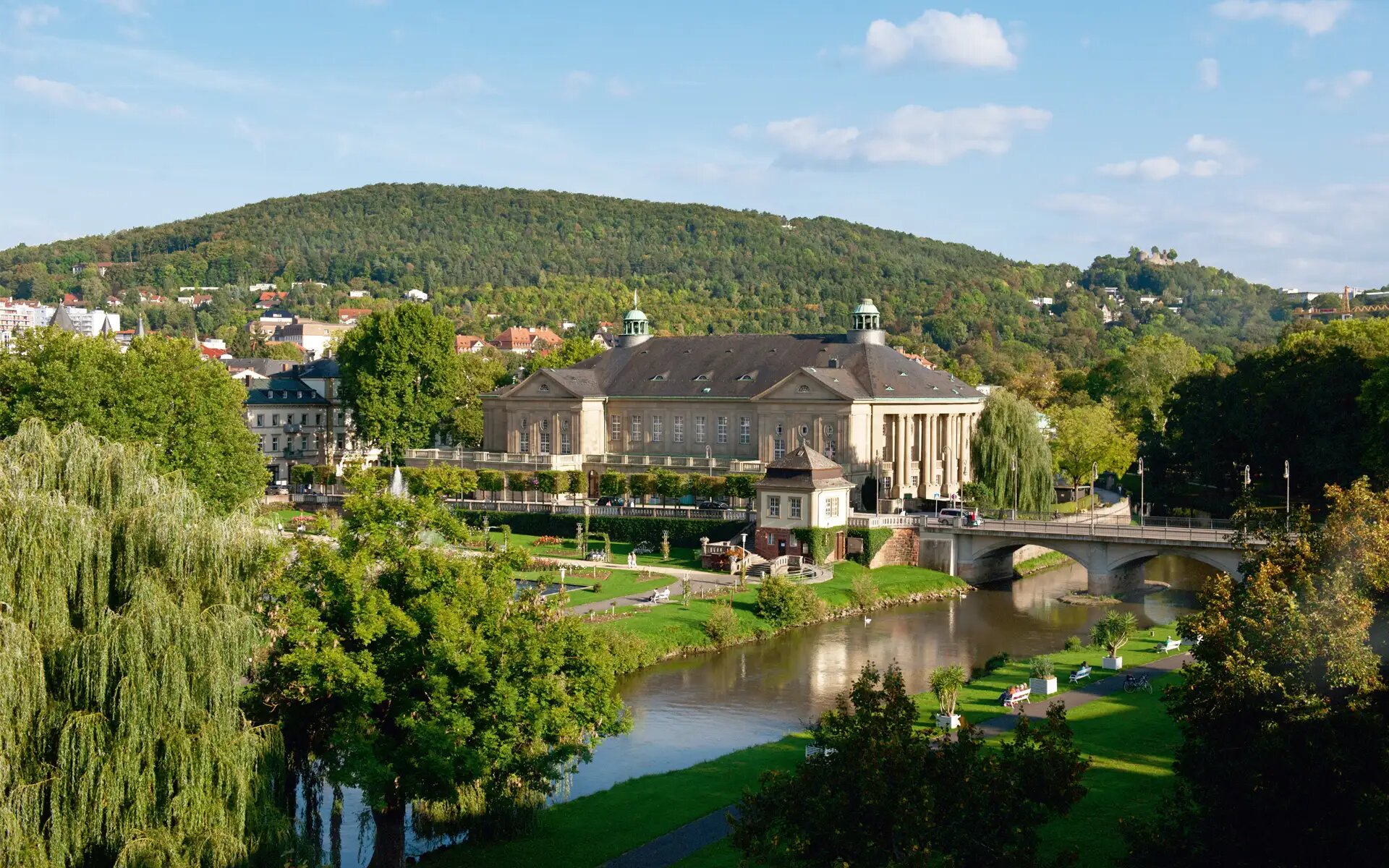 Stadtansicht mit historischer Architektur, Fluss und gruener Landschaft.