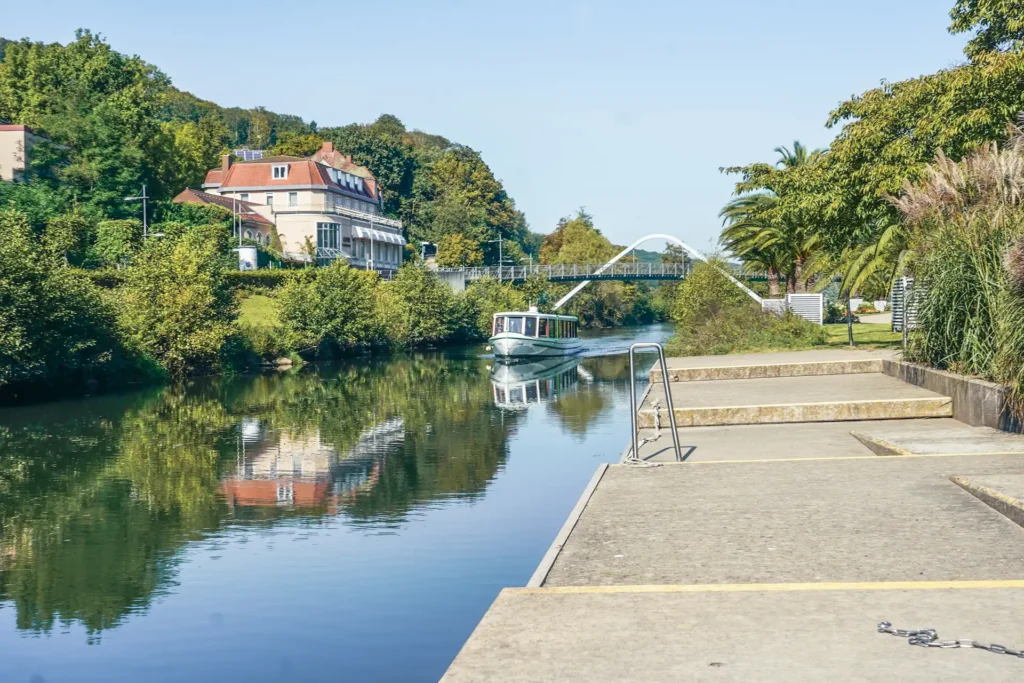 Boot „Saline“ fährt auf ruhigem Fluss, moderne Brücke im Hintergrund.