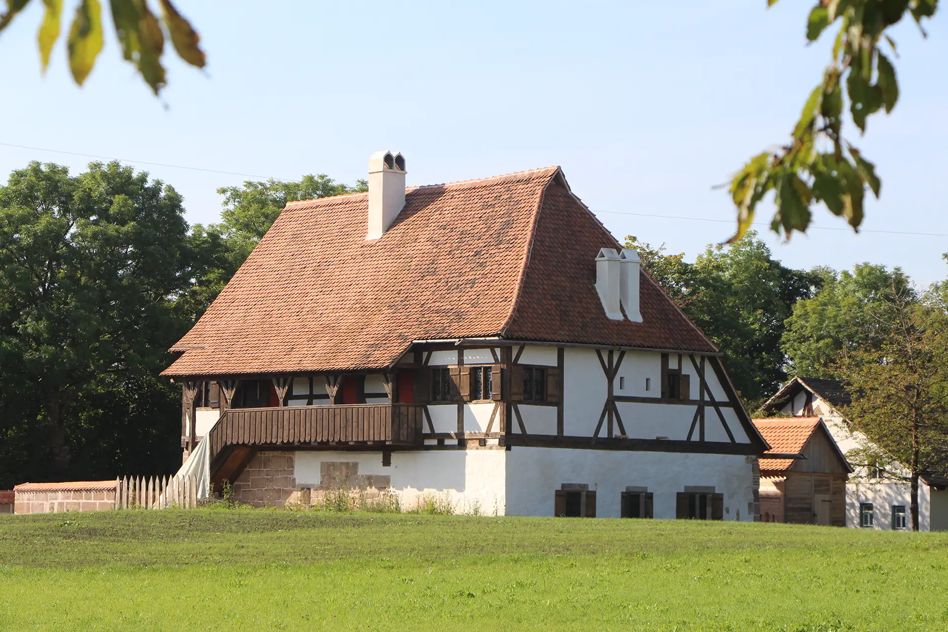 Fachwerkhaus mit rotem Ziegeldach, umgeben von grüner Wiese und Bäumen.