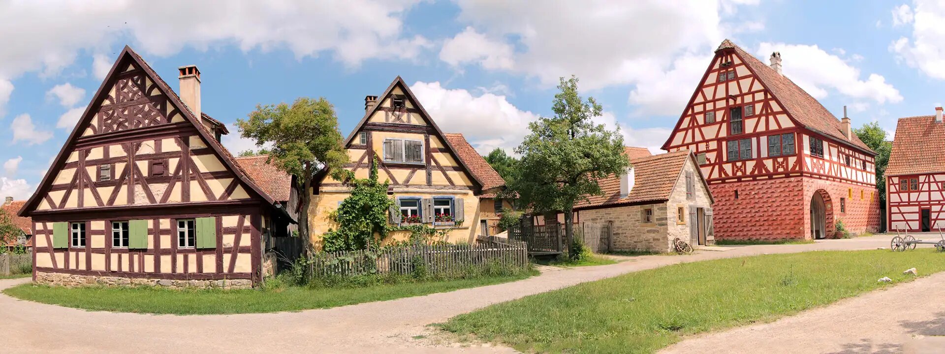 Historische Fachwerkhäuser mit grünen Fensterläden, roten Ziegeldächern, ländliche Umgebung, blauer Himmel.