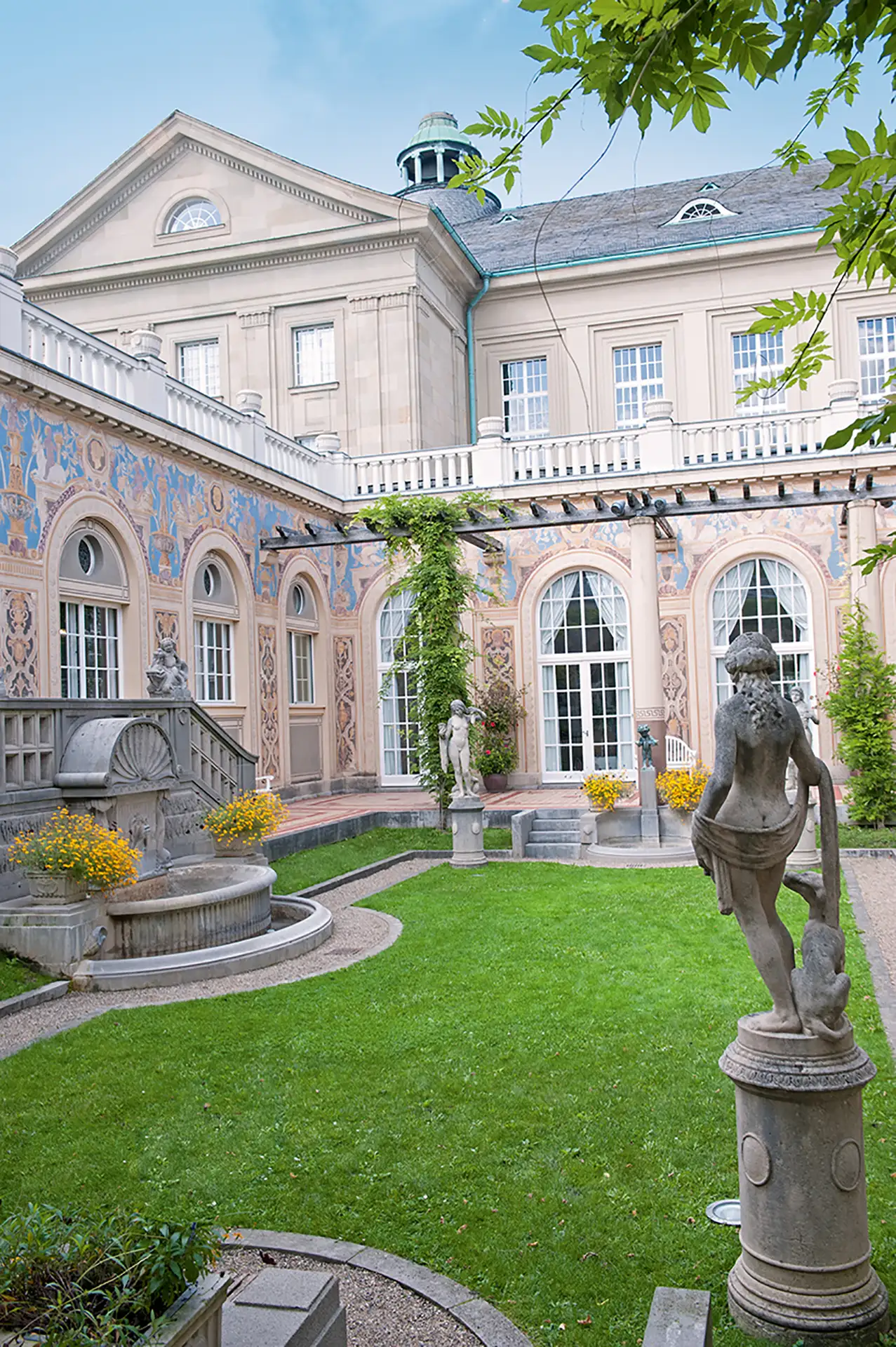 Ansicht des Innenhofs des Regentenbaus mit grünem Rasen und Statuen.