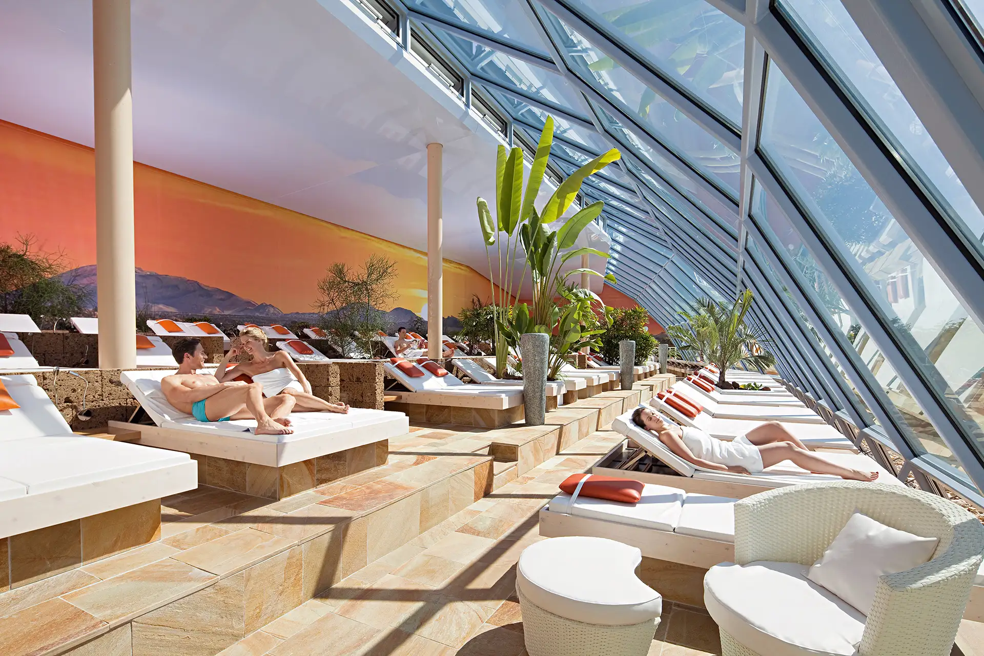 Sonnenlounge, tropische Pflanzen, Entspannung, Panorama-Dach, gemütliche Liegen, warmes Ambiente.