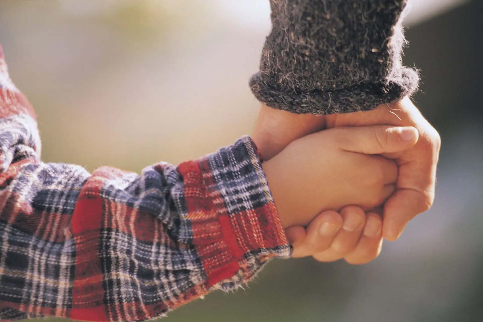 Bindungsstörung Ein Kind hält die Hand eines Erwachsenen in einer fürsorglichen Geste.