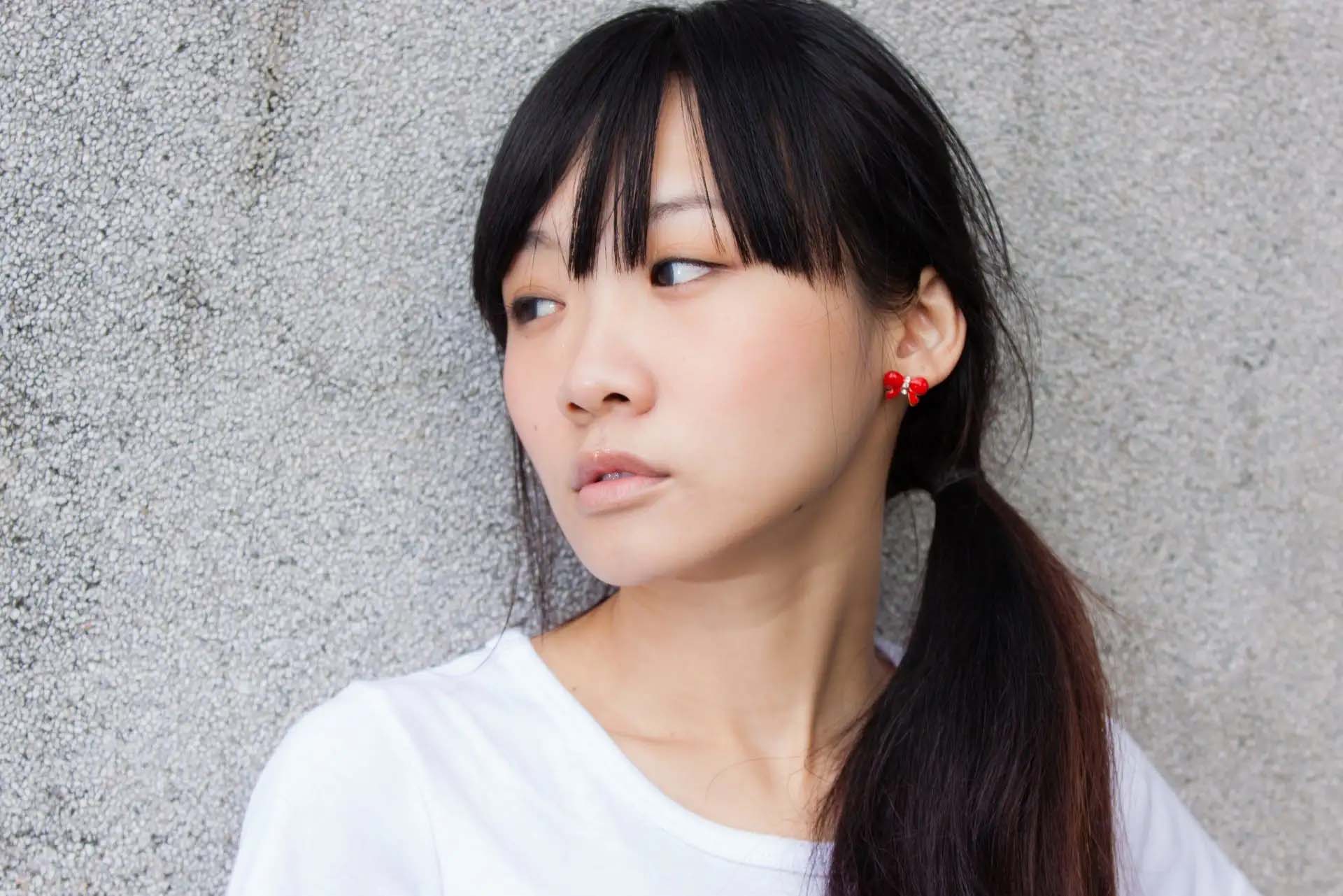 Eine junge Frau mit rotem Ohrschmuck schaut nachdenklich zur Seite.