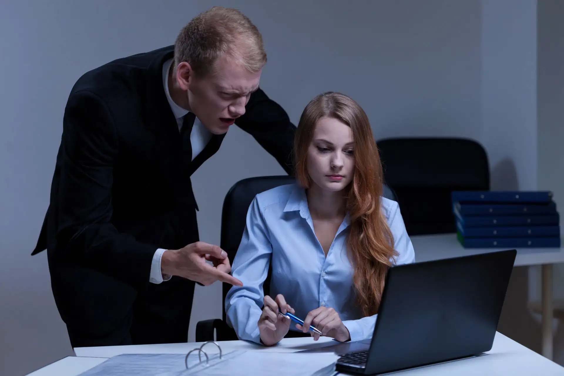 Ein Mann in einem Anzug scheint eine Frau am Arbeitsplatz streng zu kritisieren.