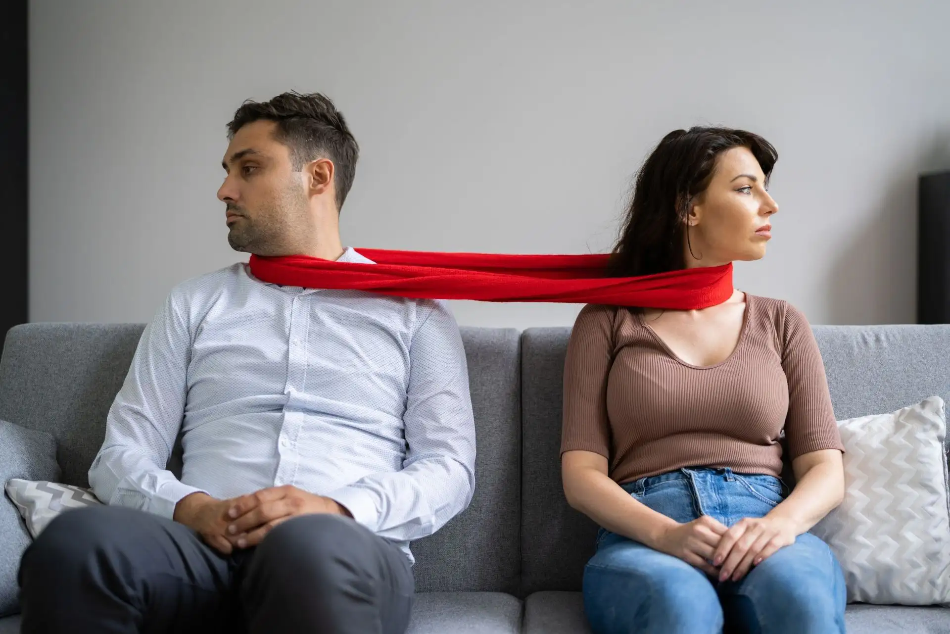Ein Paar sitzt auf einem Sofa, verbunden durch einen roten Schal.