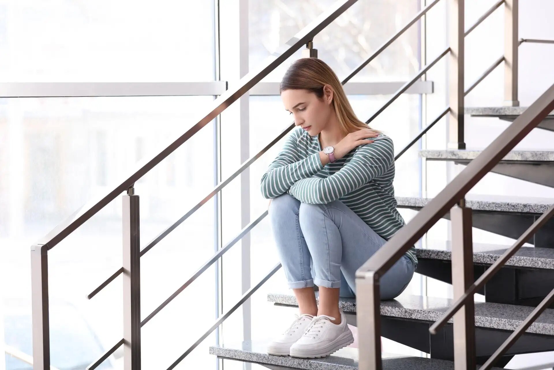 Eine nachdenkliche Frau sitzt allein auf einer Treppe, Arme verschränkt.