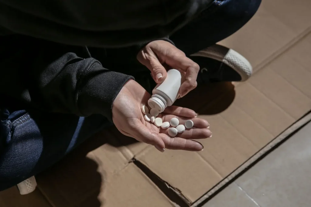 Person hält Tablettenflasche, schüttet weiße Pillen in die Hand.