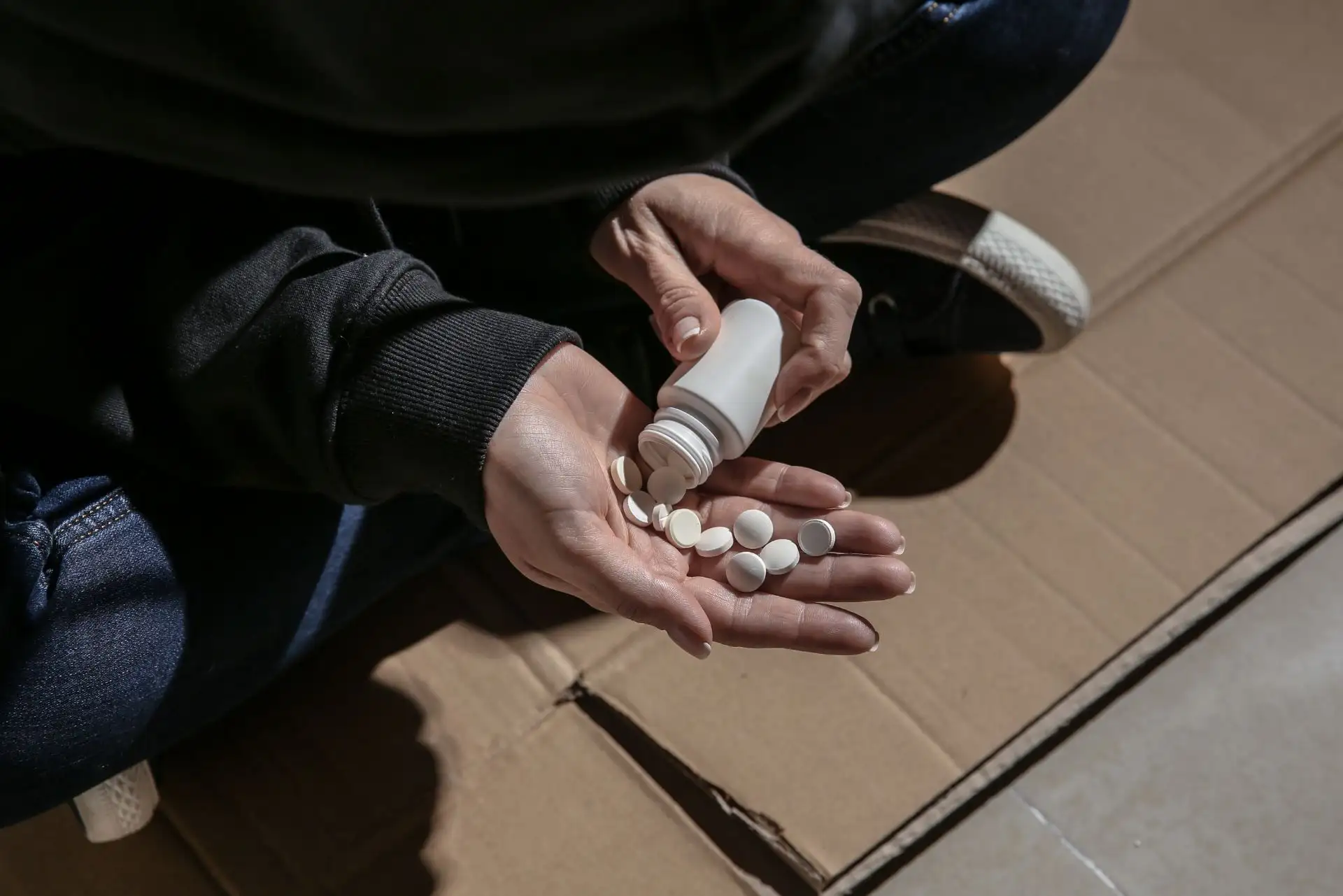 Person hält Tablettenflasche, schüttet weiße Pillen in die Hand.