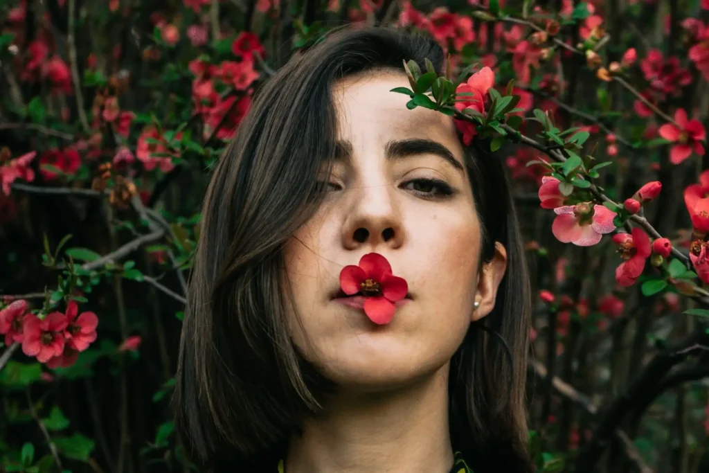 Frau mit Blüte im Mund vor blühendem Busch.
