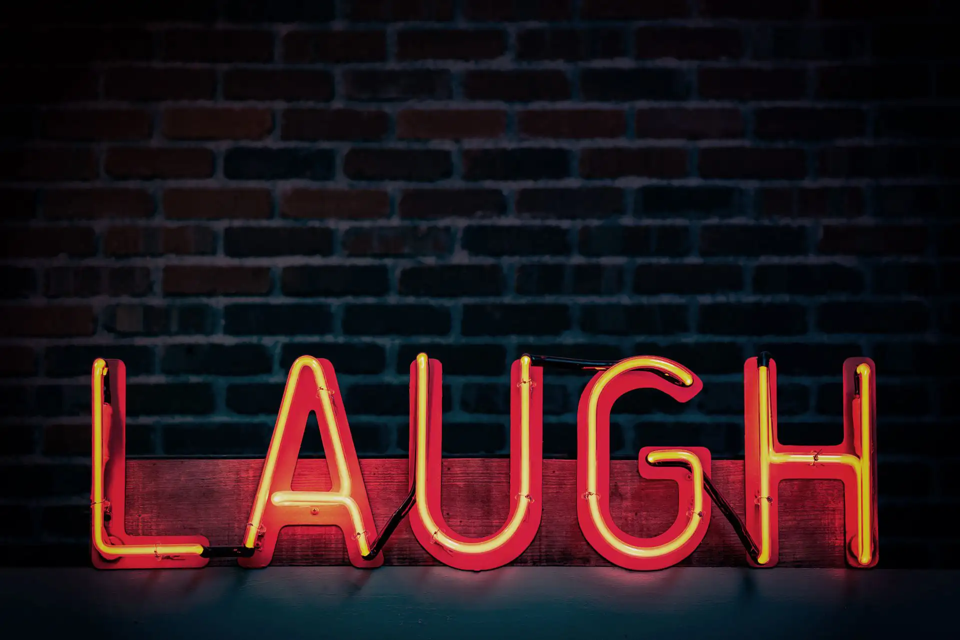 Neon-Schriftzug „LAUGH“ vor einer Ziegelwand.