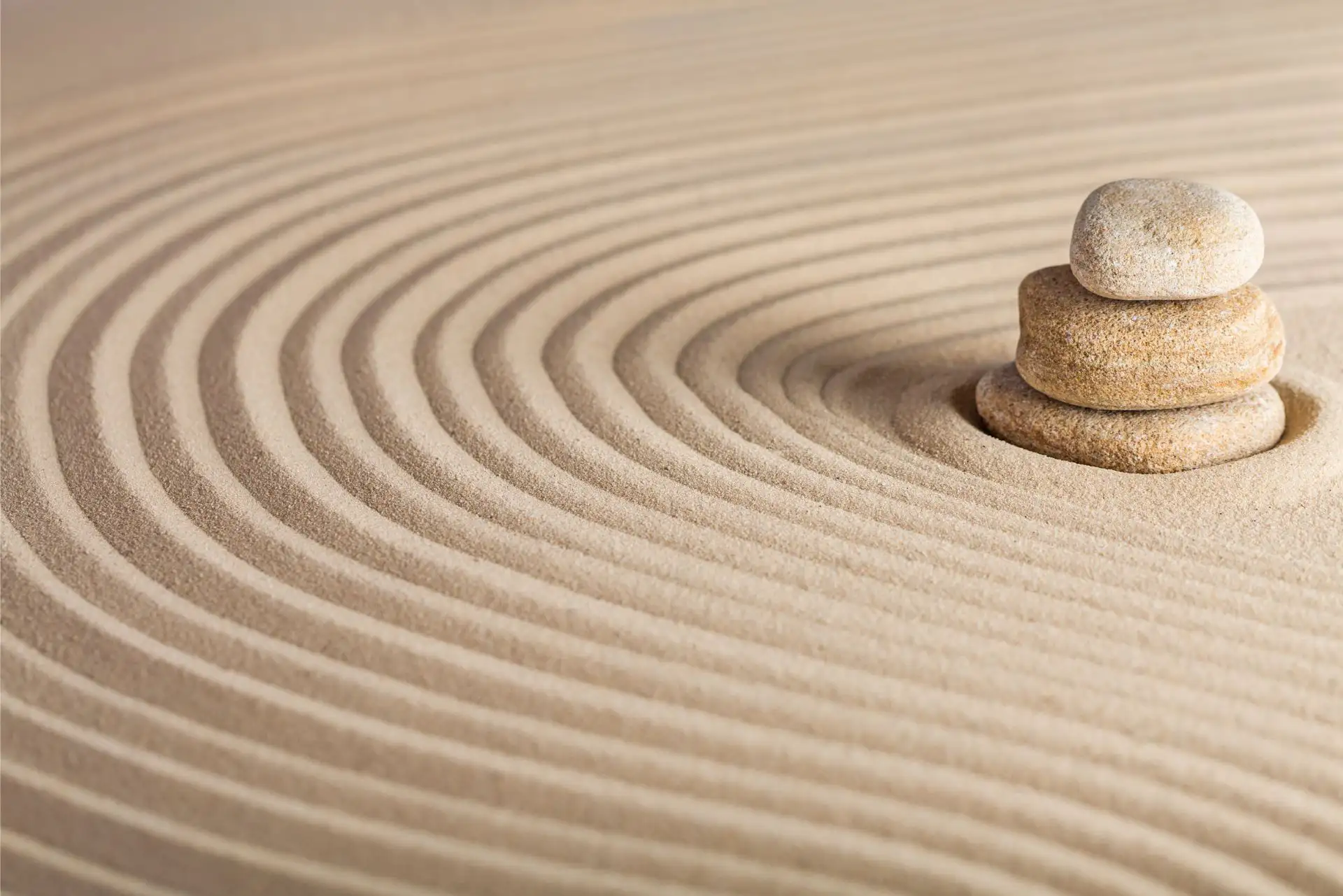 Zen-Garten mit Steinen und wellenförmigen Linien im Sand.