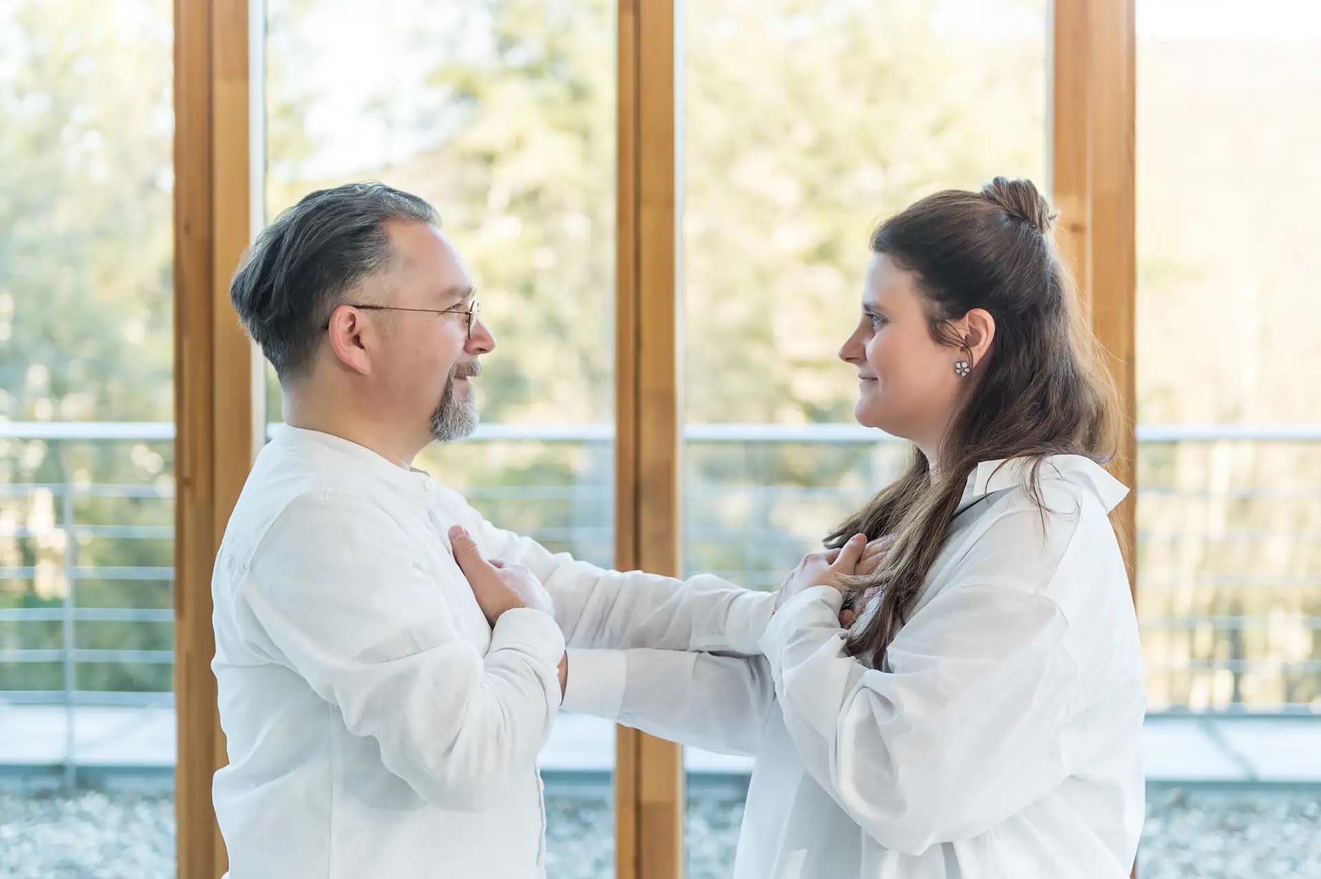 Zwei Personen in weißer Kleidung berühren gegenseitig ihre Brust respektvoll.