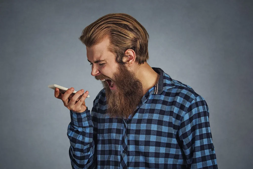 Ein Mann schreit wütend in sein Telefon, voller Frustration.