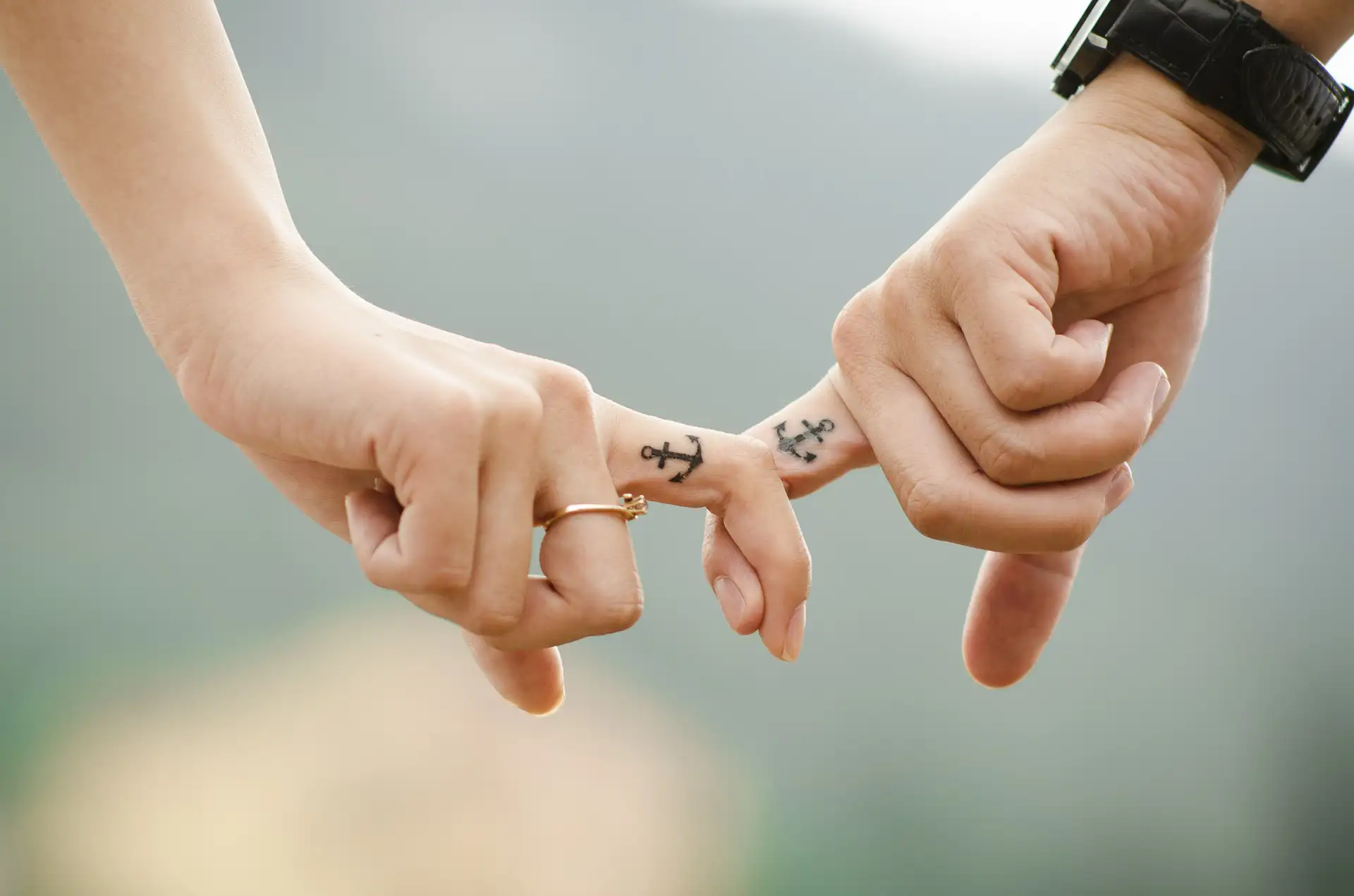 Zwei Hände mit Anker-Tattoos halten sich an den kleinen Fingern.
