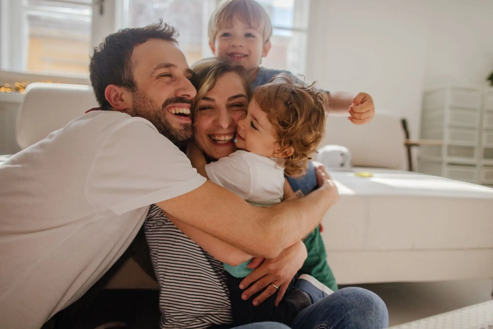Eine glückliche Familie umarmt sich herzlich in einem gemütlichen Wohnzimmer.