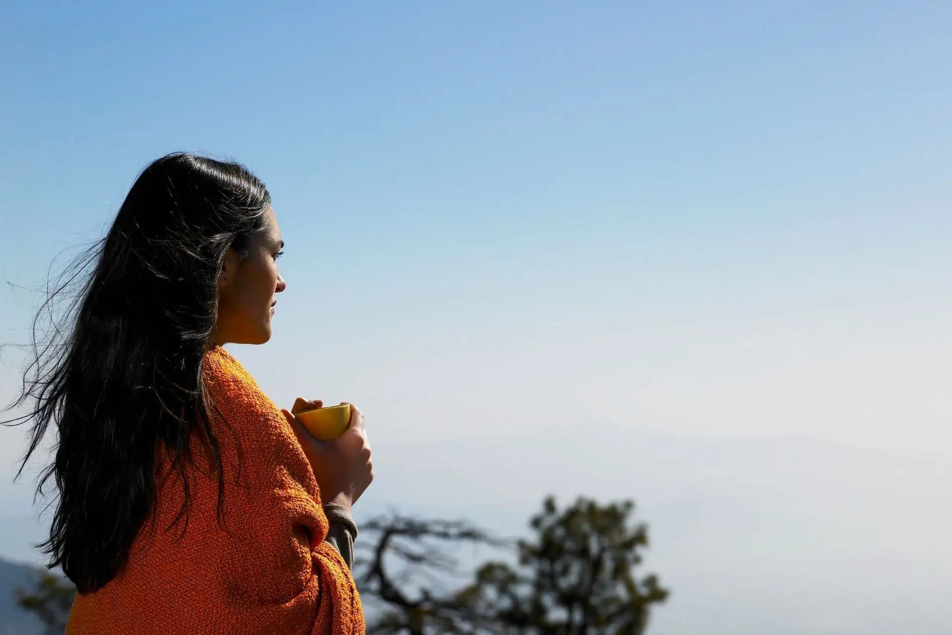 Eine Frau genießt den Ausblick, eingehüllt in eine orangefarbene Decke.