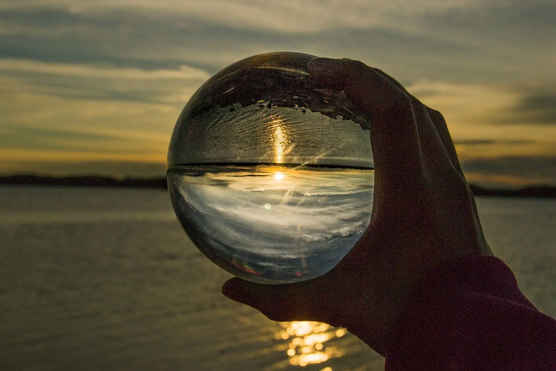 Sonnenuntergang spiegelt sich in einer Glaskugel, gehalten von einer Hand.