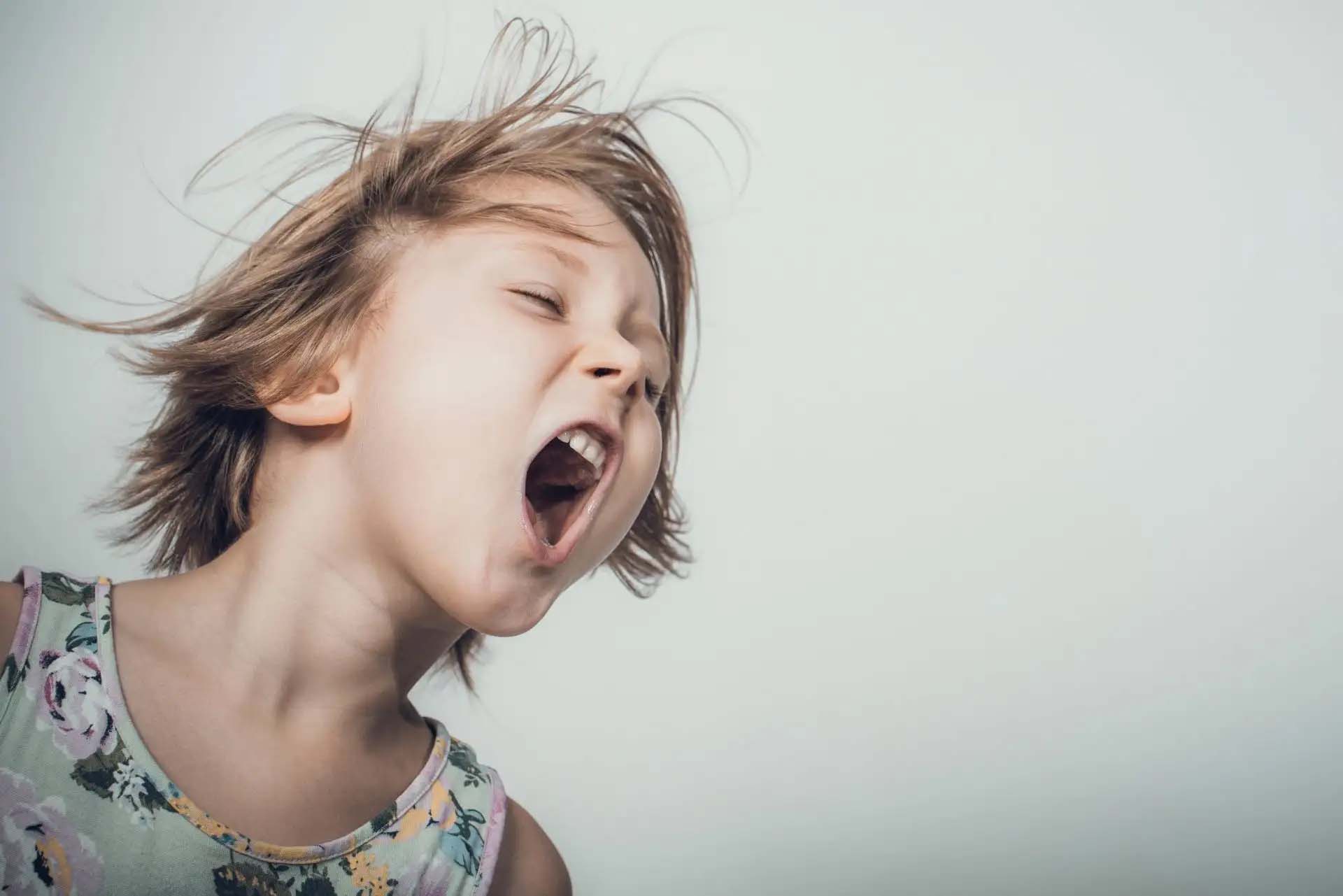 Kind schreit mit offenem Mund, Haare fliegen in Bewegung. Aggressionen bei Kindern