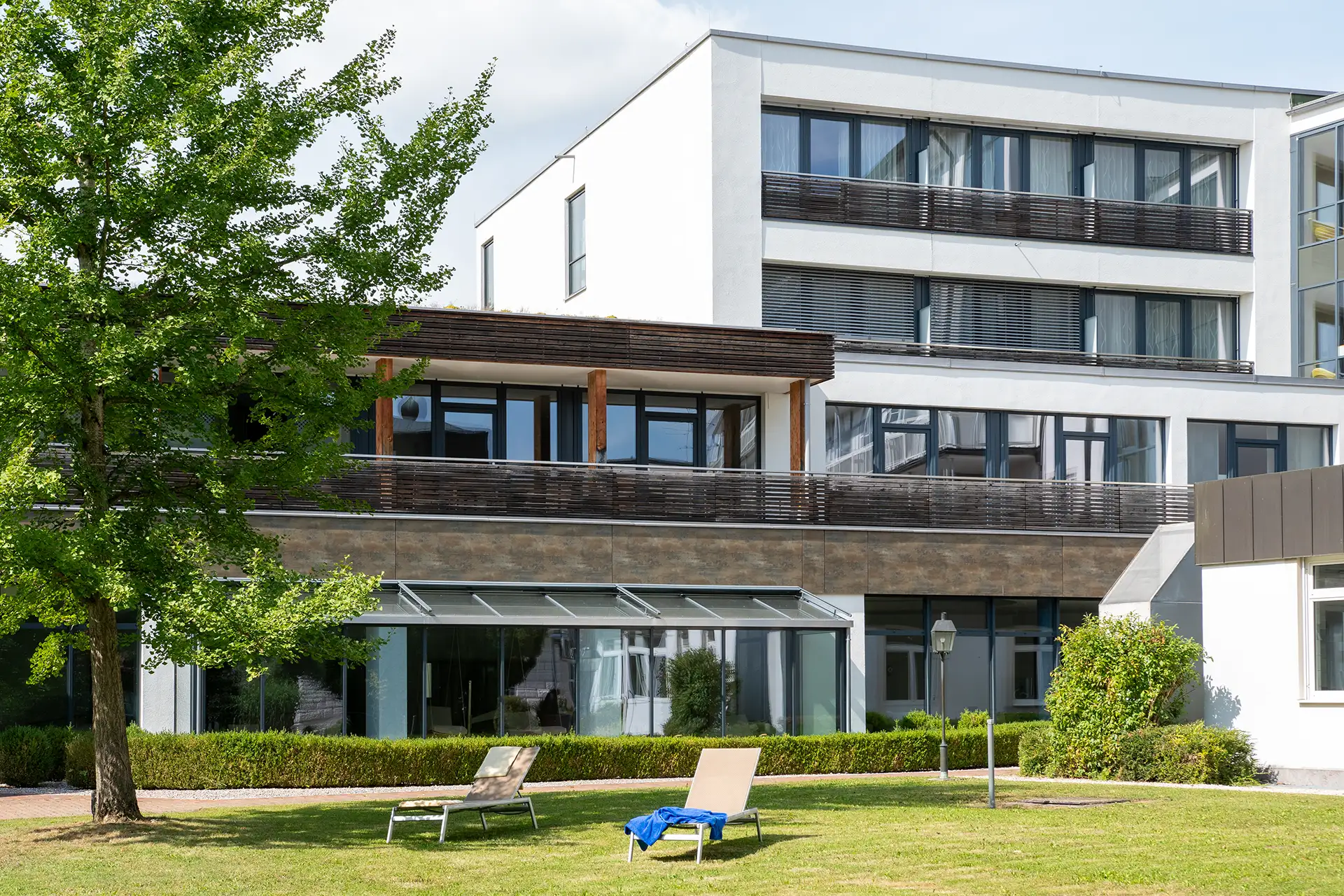 Moderner Gebaeudekomplex mit gruener Gartenanlage und Sonnenliegen im Vordergrund.