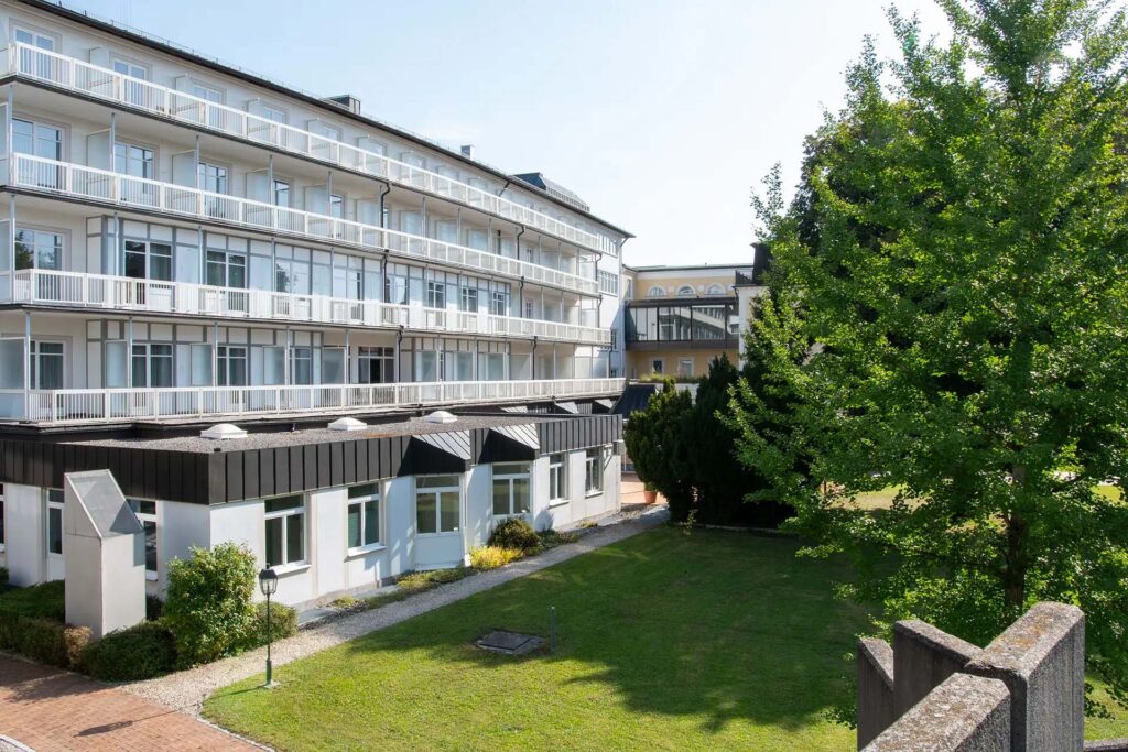 Modernes Gebaeude mit Balkonen und gruener Gartenanlage bei sonnigem Wetter.