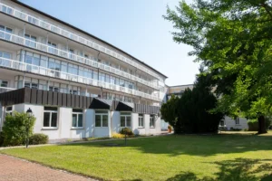 Modernes Gebäude mit Balkonen und grüner Gartenanlage bei sonnigem Wetter.