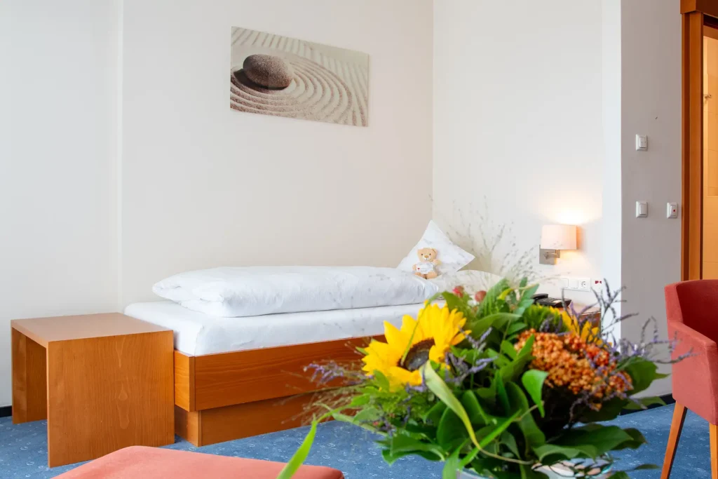 Helles, gemütliches Zimmer mit Einzelbett, Blumenstrauß und dekorativem Wandbild.