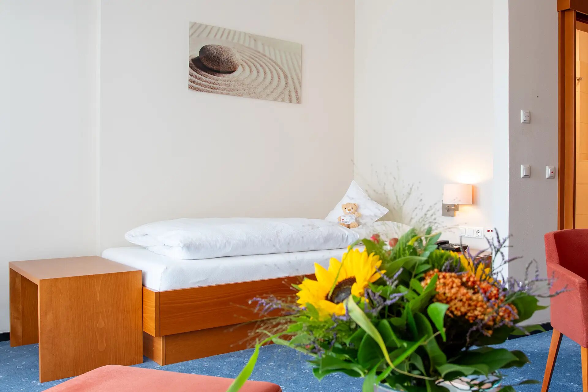 Helles, gemütliches Zimmer mit Einzelbett, Blumenstrauß und dekorativem Wandbild.