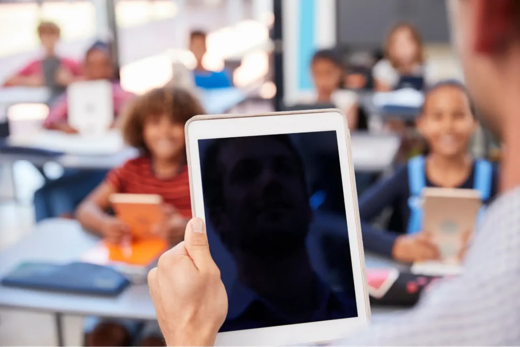 Lehrer hält Tablet vor Schülern in modernem Klassenzimmer mit digitalem Unterricht.