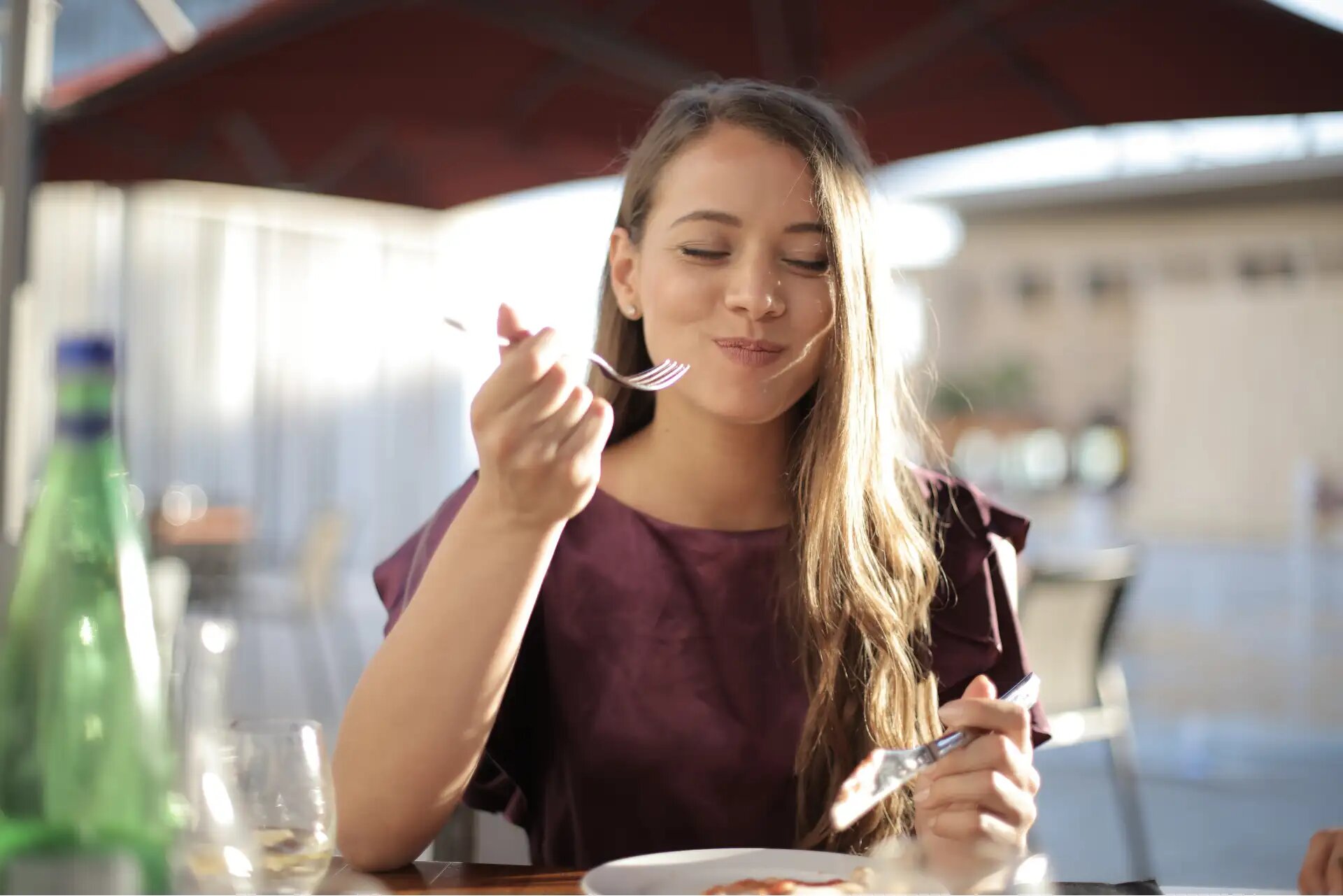 Glückliche Frau genießt ihr Essen in einem sonnigen Außenrestaurant.