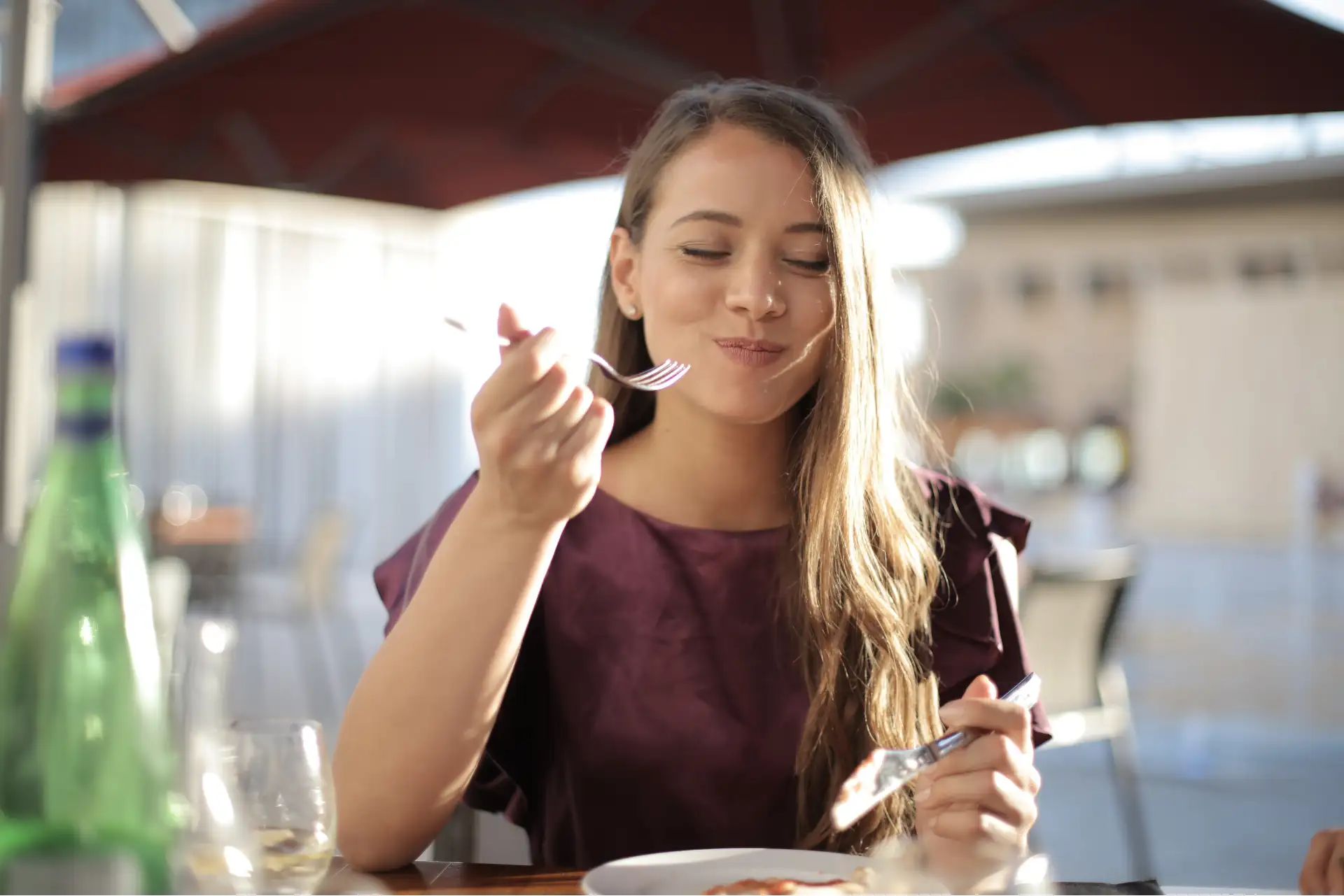 Glückliche Frau genießt ihr Essen in einem sonnigen Außenrestaurant.