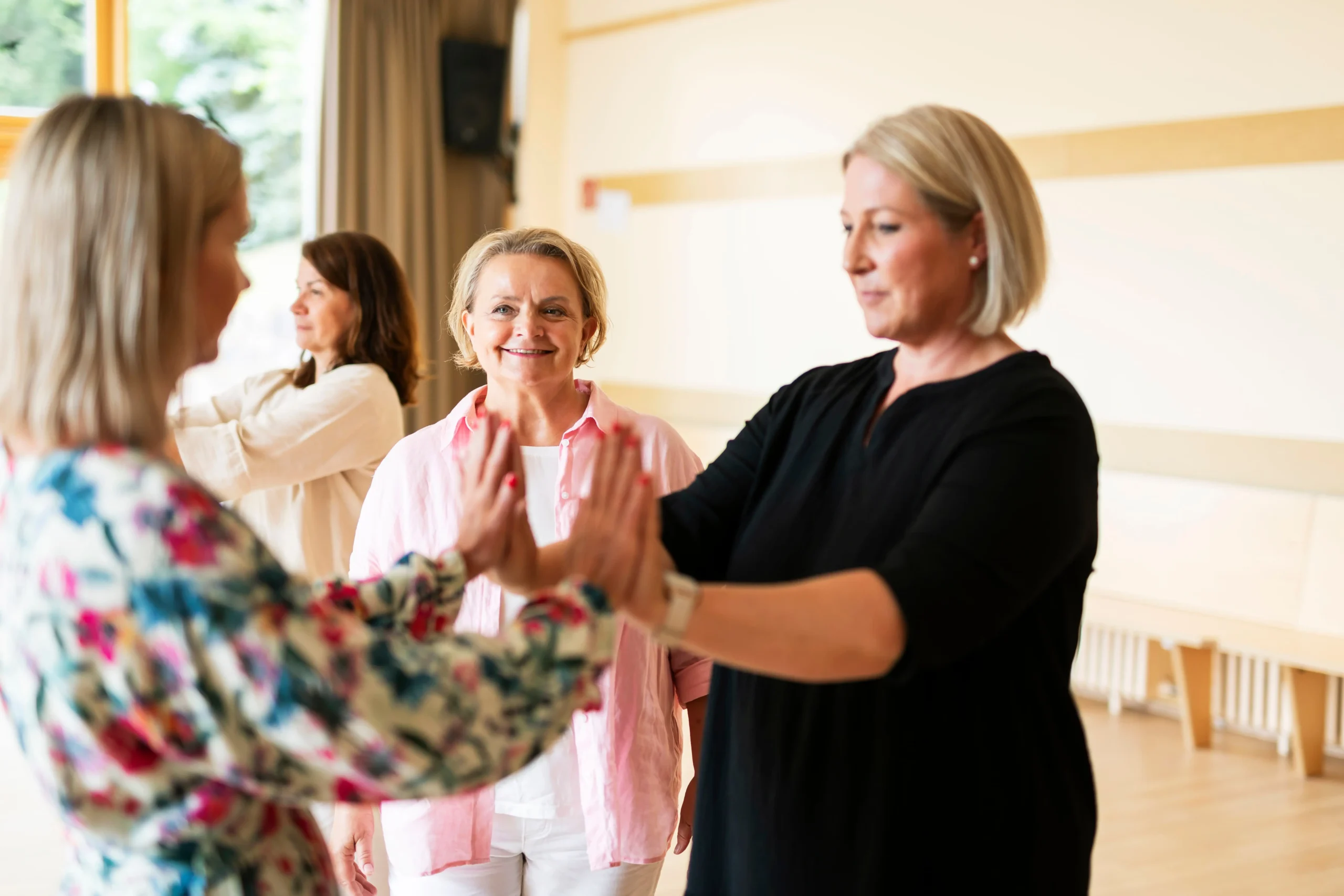 Zwei Frauen berühren sich mit den Handflächen, eine weitere Frau lächelt und leitet sie an.