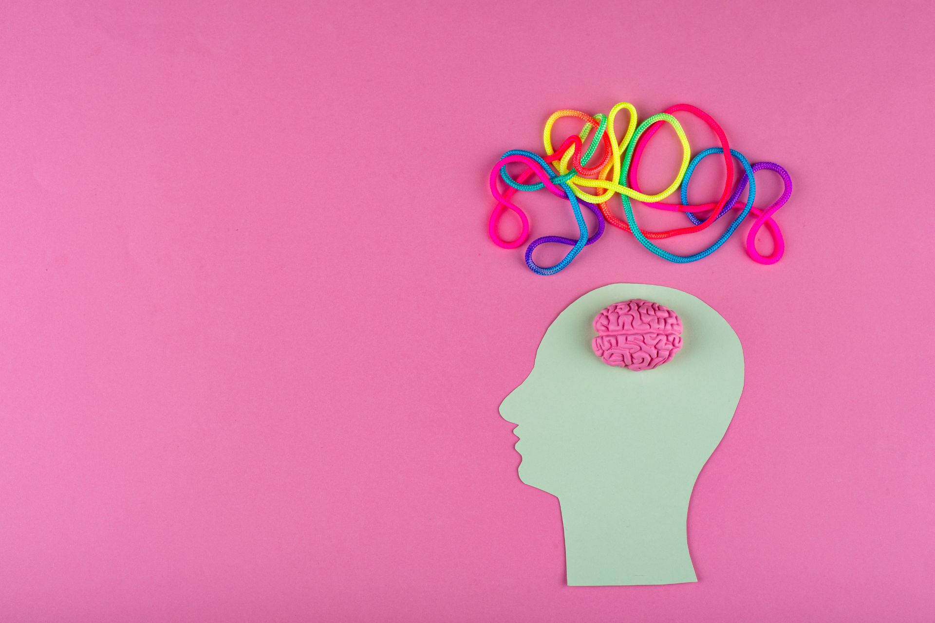 Neurodivergenz symbolisiert: stilisierte Kopf-Silhouette mit Gehirn und bunten Schnüren auf rosa Hintergrund.