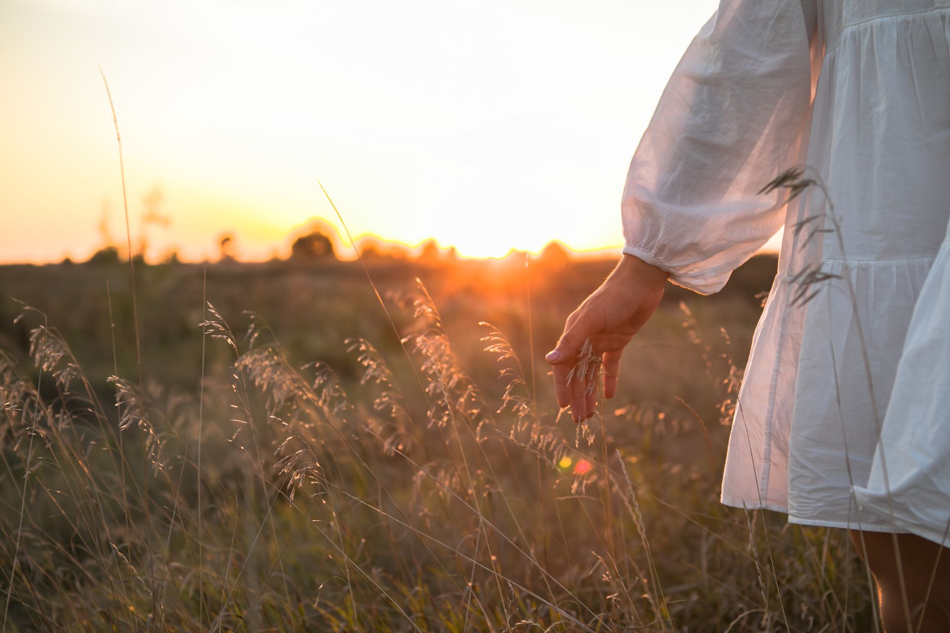 Frau in einem weißen Kleid auf einer Wiese bei Sonnenuntergang in Stille.