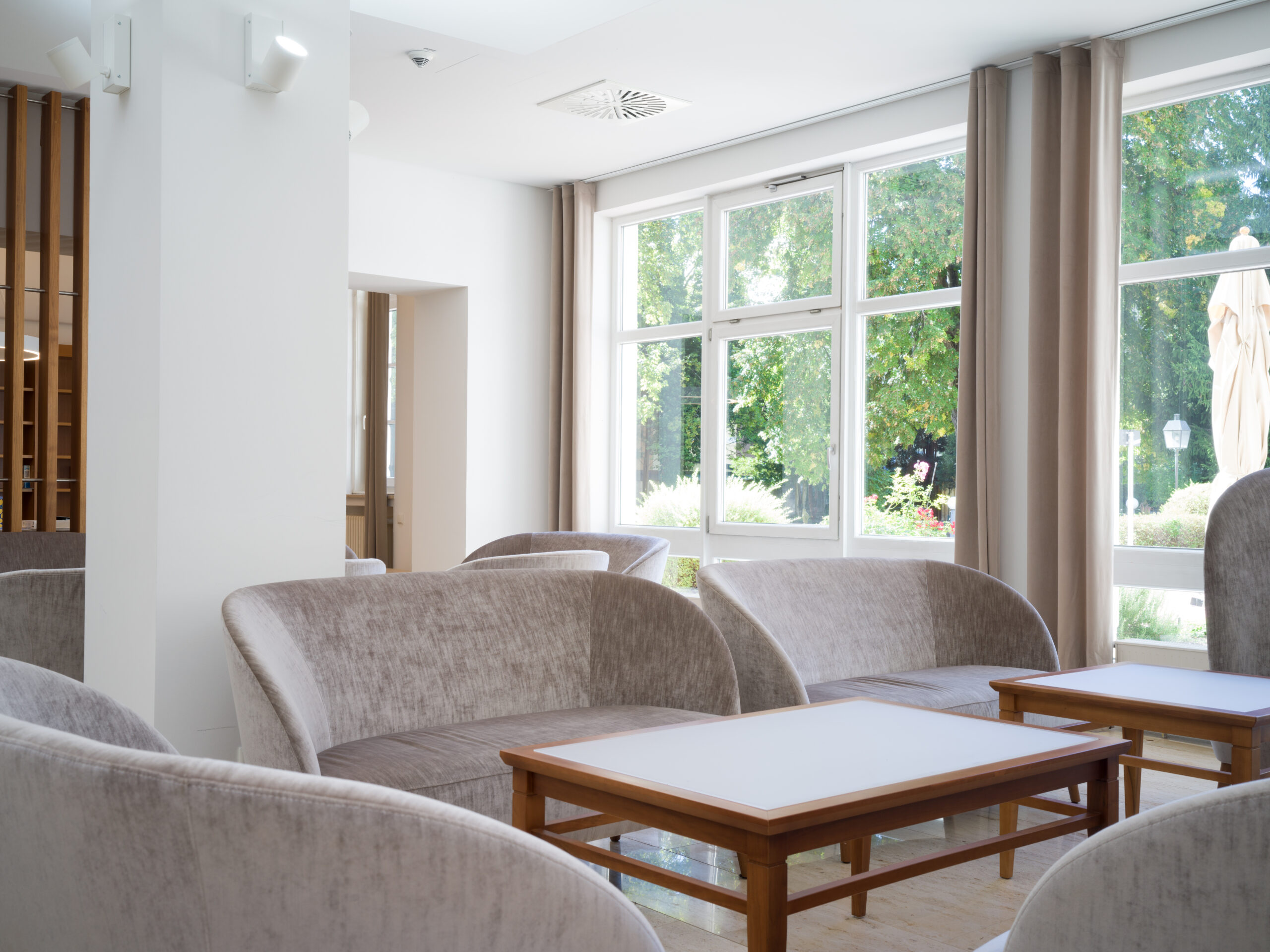 Ansprechender Aufenthaltsraum mit Sofas und Tischen vor einer hellen Fensterfront.