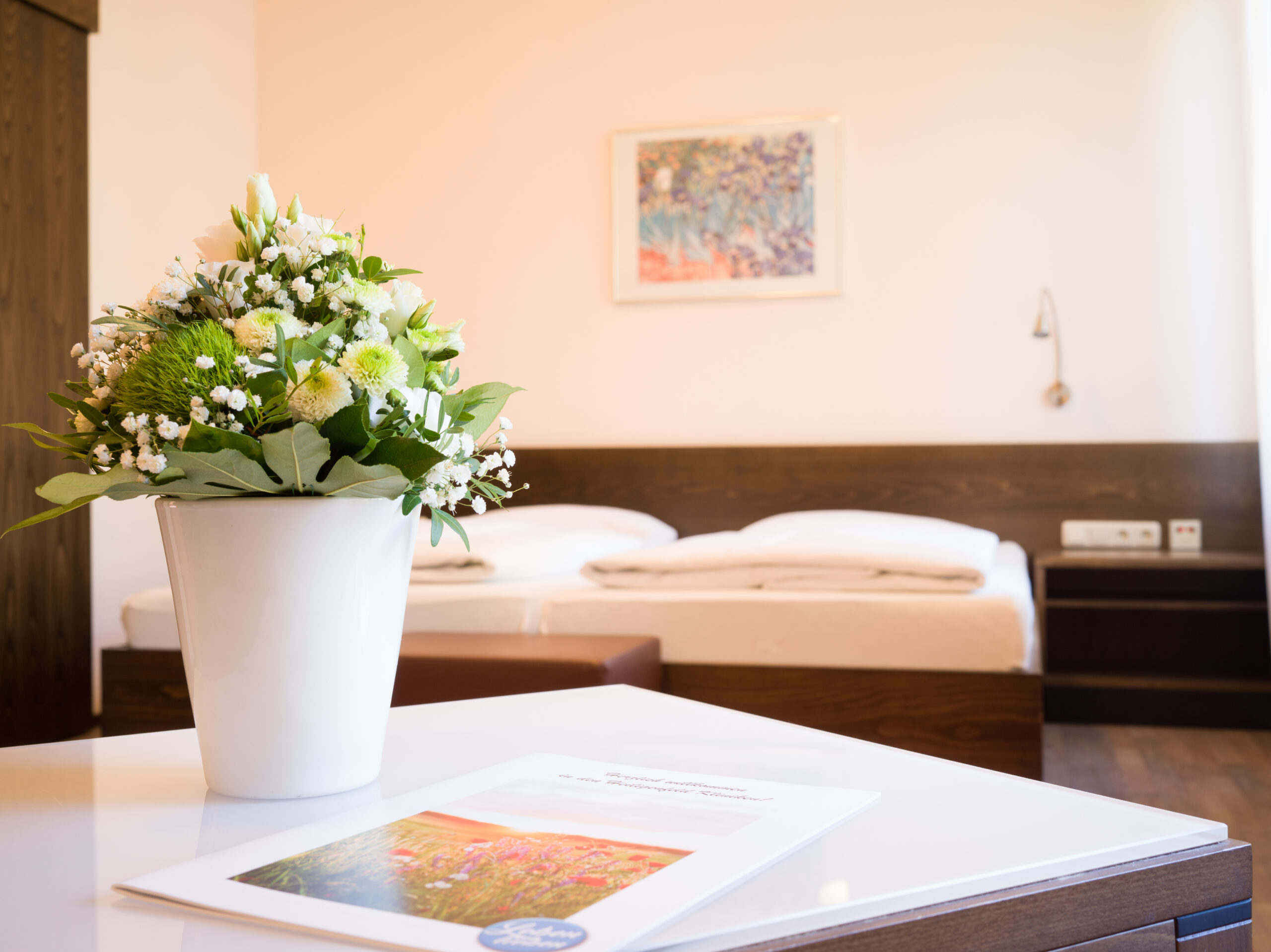 Ansicht eines ansprechenden Zweibettzimmers mit einem schönen Blumenstraus auf dem Tisch